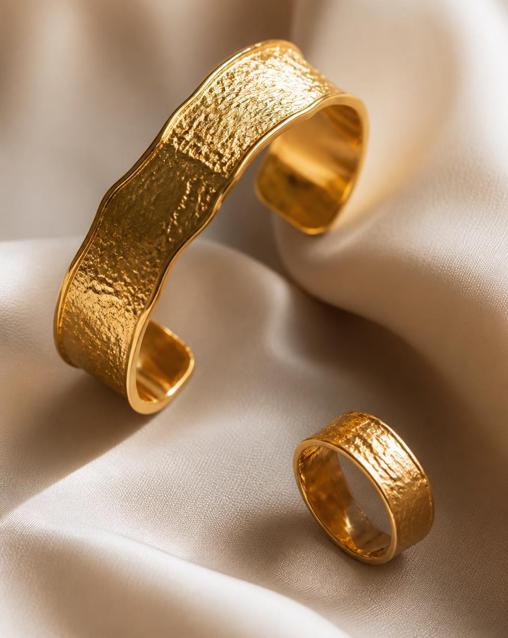 Textured 18K gold cuff and ring resting on ivory silk